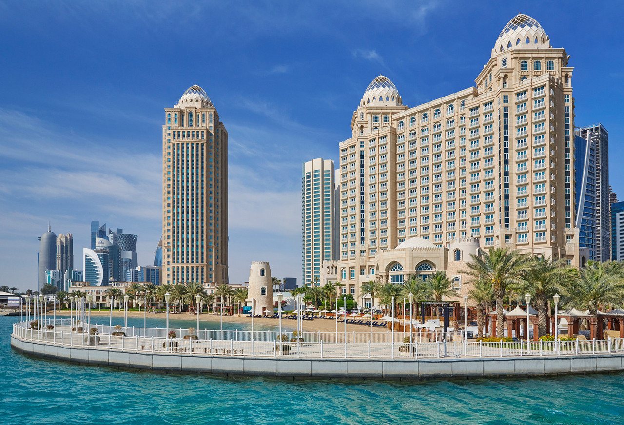Four Seasons Hotel Doha seen from the water, twin towers above a palm-lined waterfront