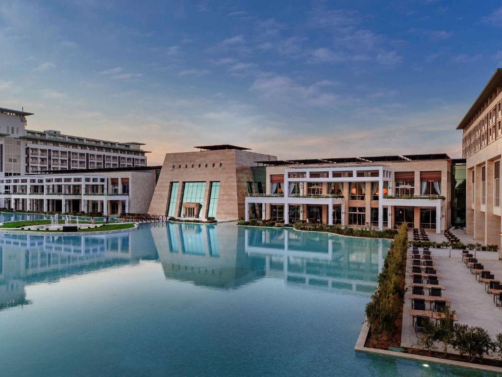 Rixos Premium Antalya resort buildings reflected in a still pool at dusk